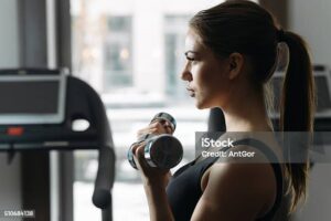 Beautiful woman lifting dumbbell in gym. She training biceps.